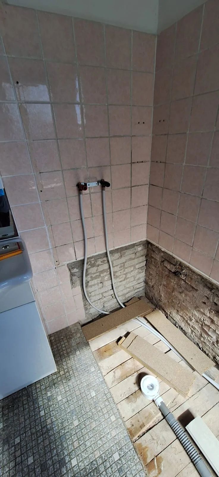 Badkamer tijdens de sloop met de vloer open tot de houten balken en een afvoerslang