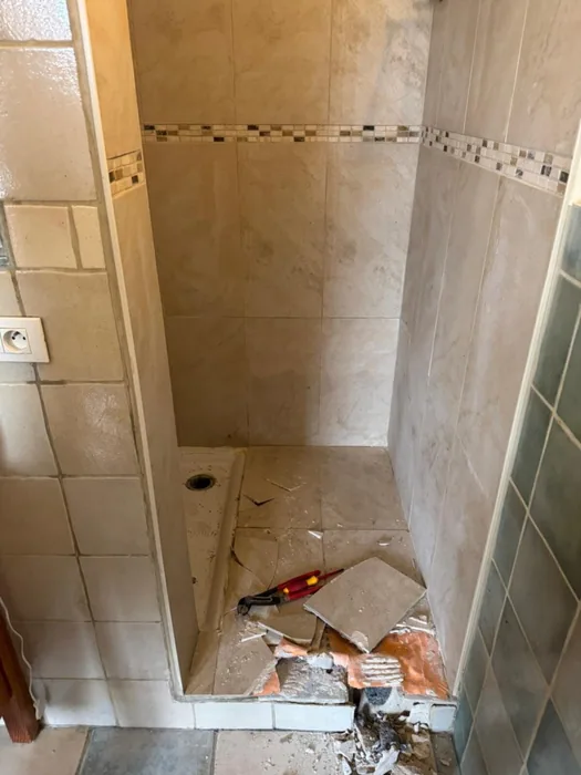 Tijdens: vloertegels uit de douche, afvoer zichtbaar, beige wandtegels met mozaïekrand