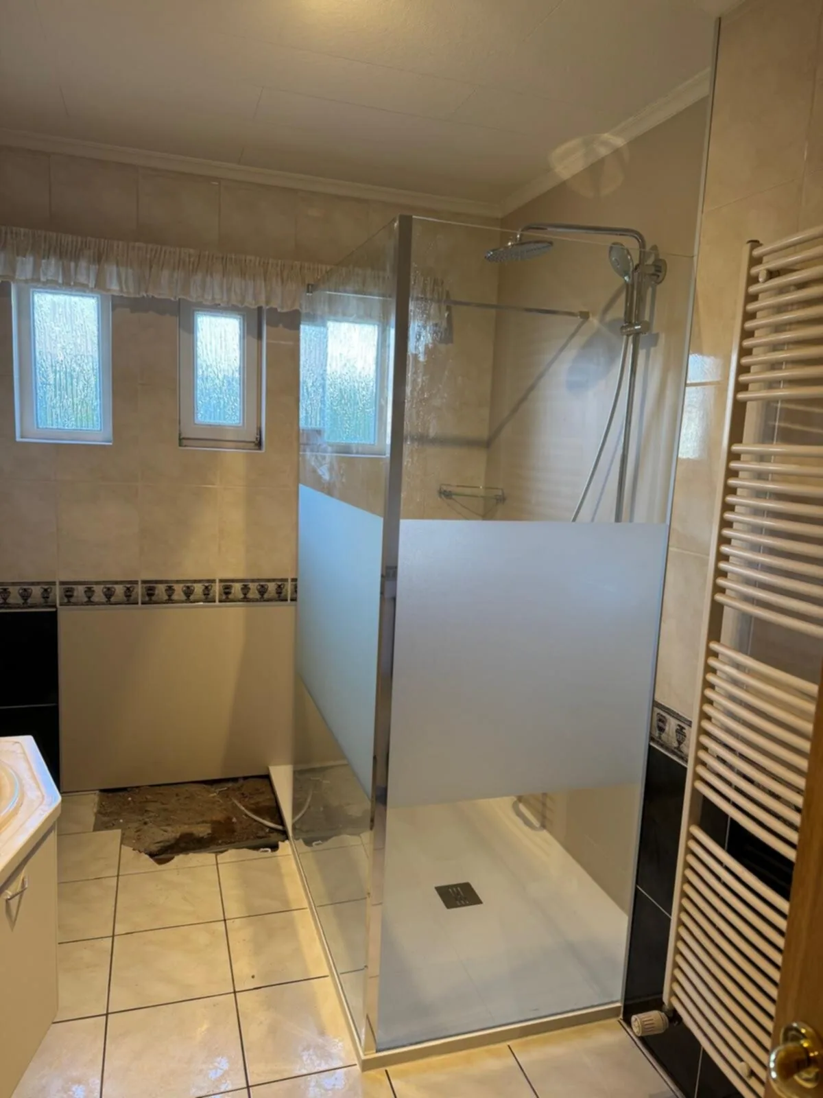 Inloopdouche met een deels matte glazen wand onder drie kleine ramen