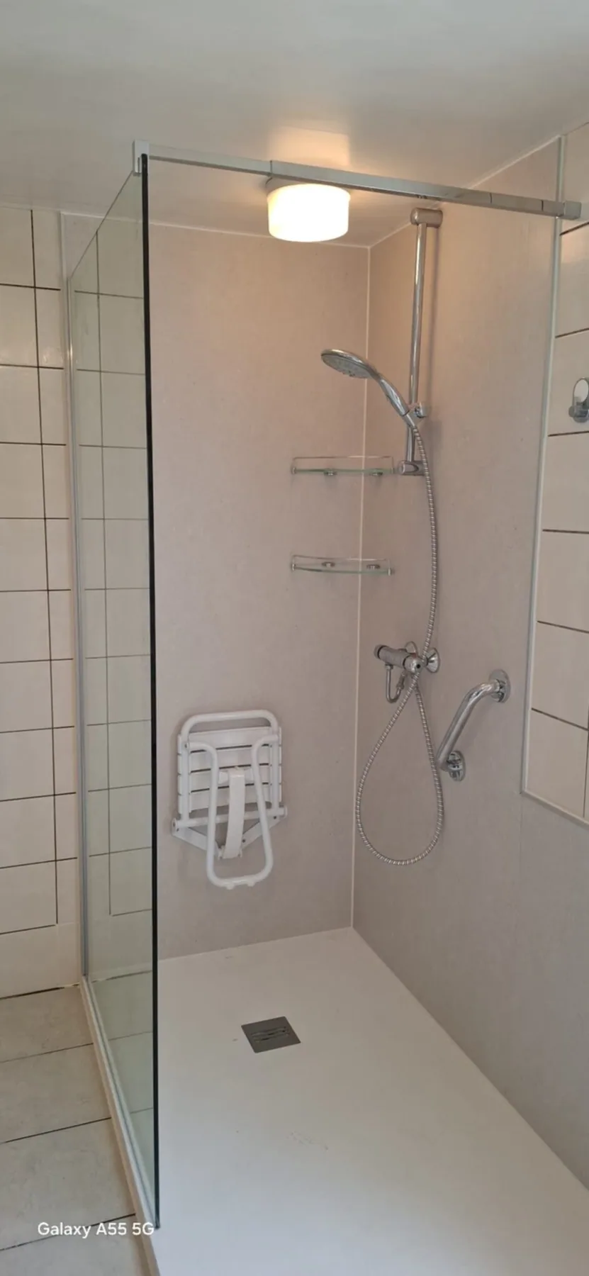 Inloopdouche met lichte wandpanelen, opklapbaar douchezitje, steunbeugel en glazen wand