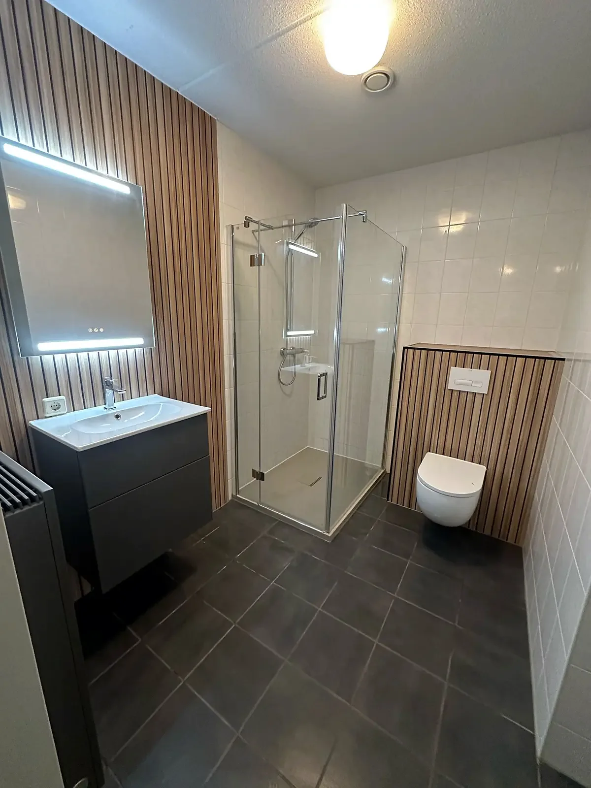 Houten lamellenwand met wastafelmeubel, ledspiegel en glazen douche