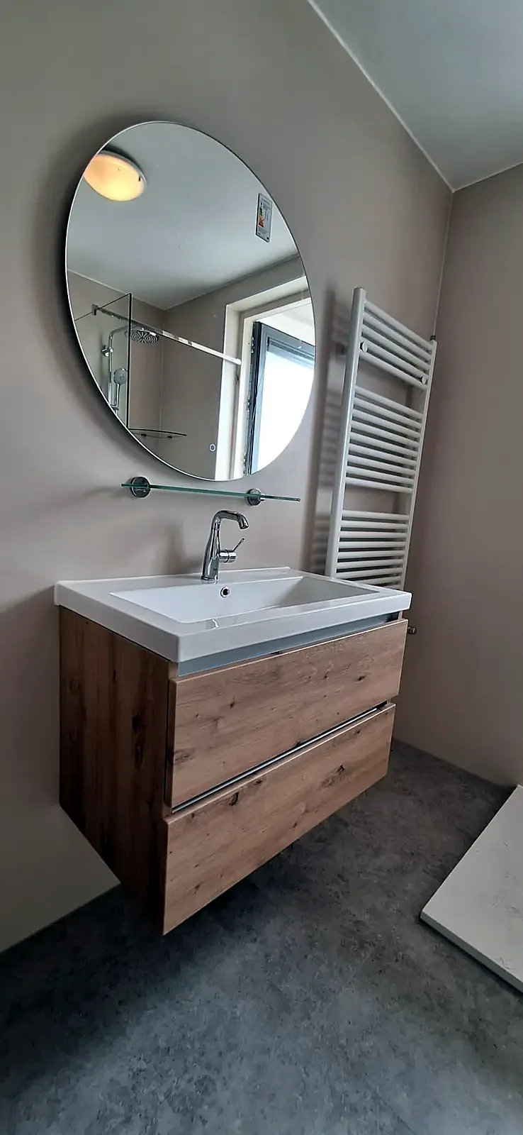 Ronde spiegel boven een houten wastafelmeubel met witte radiator